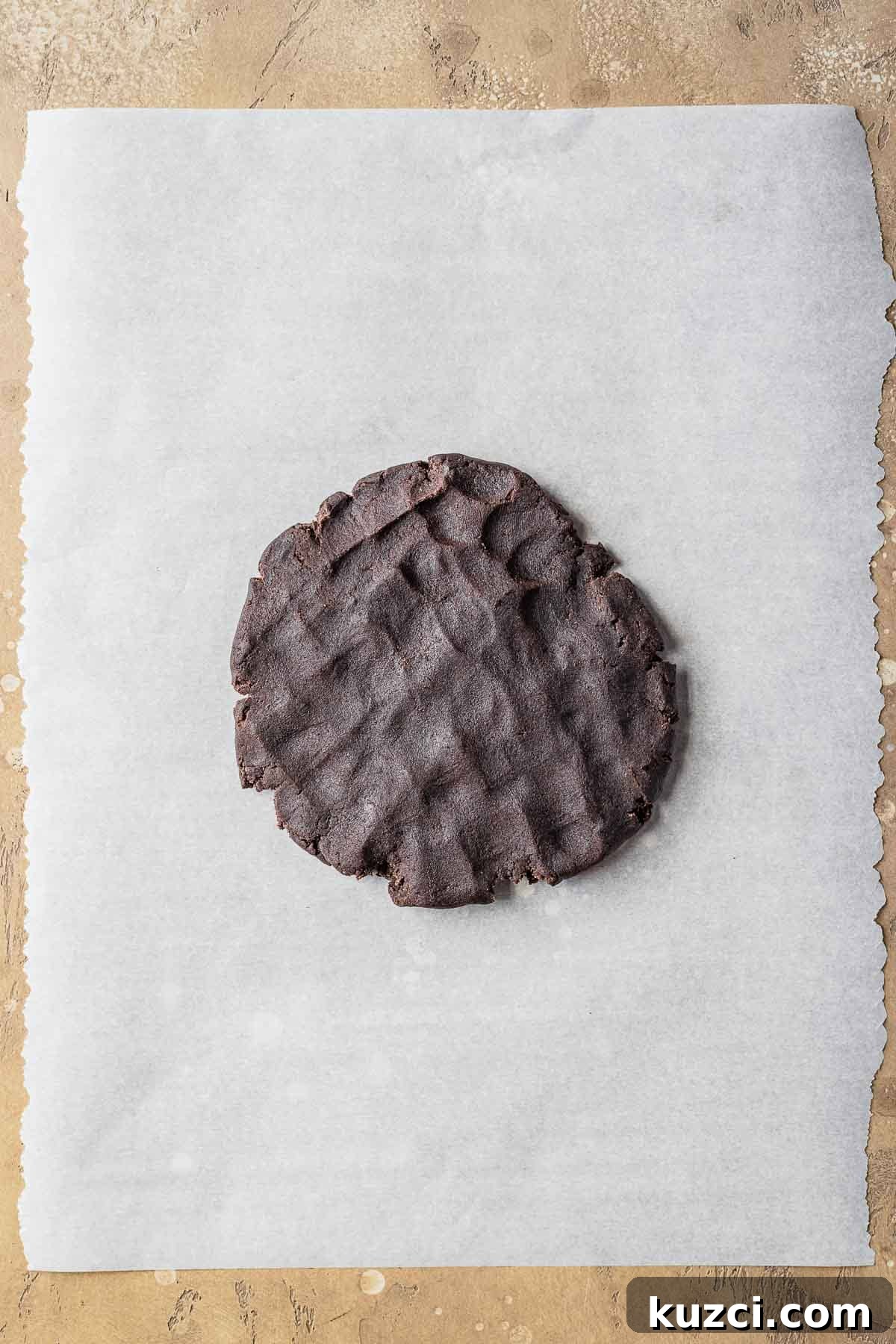 A disc of chocolate dough on parchment paper.