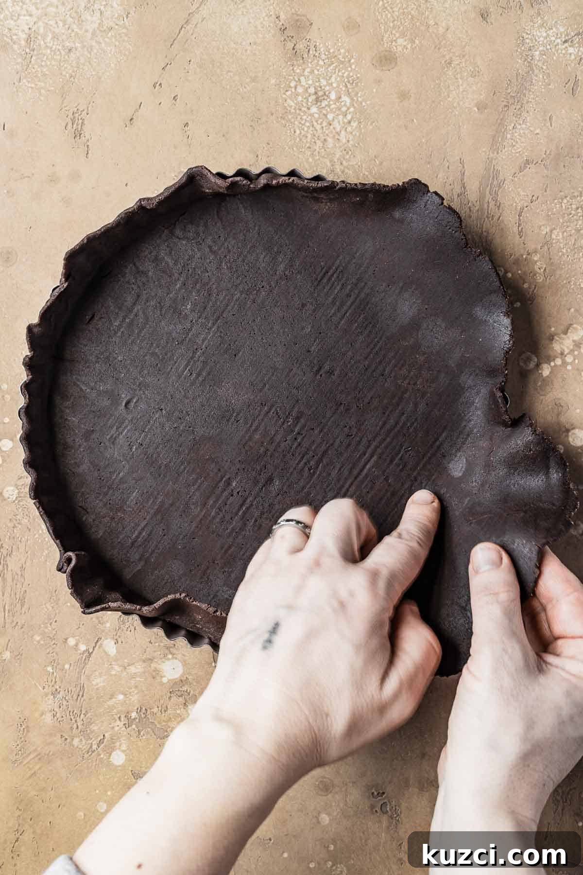 Chocolate dough being pressed into a tart pan.