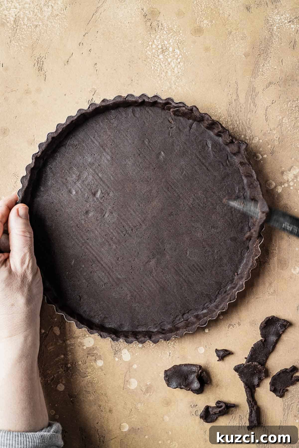 Hands trimming the edge of an unbaked tart shell with a knife.