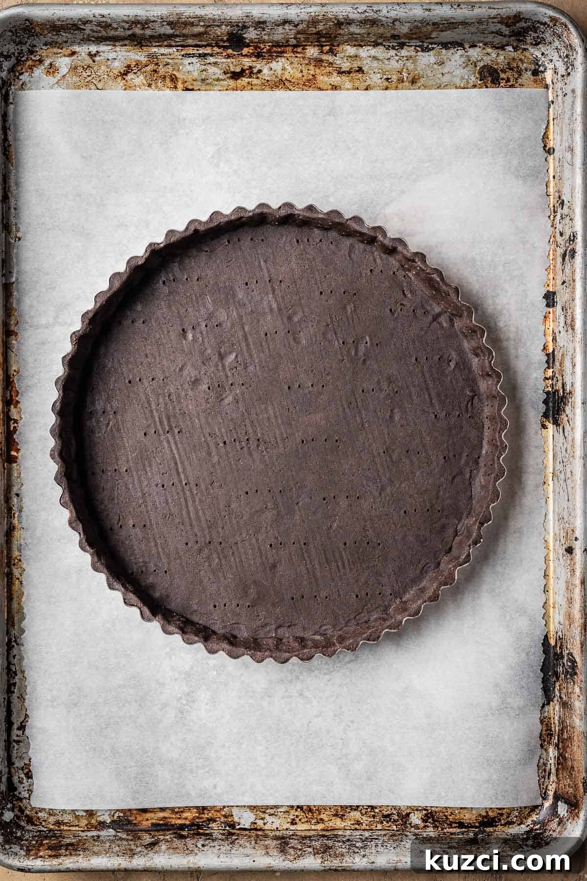An unbaked docked tart shell on a parchment lined baking sheet.