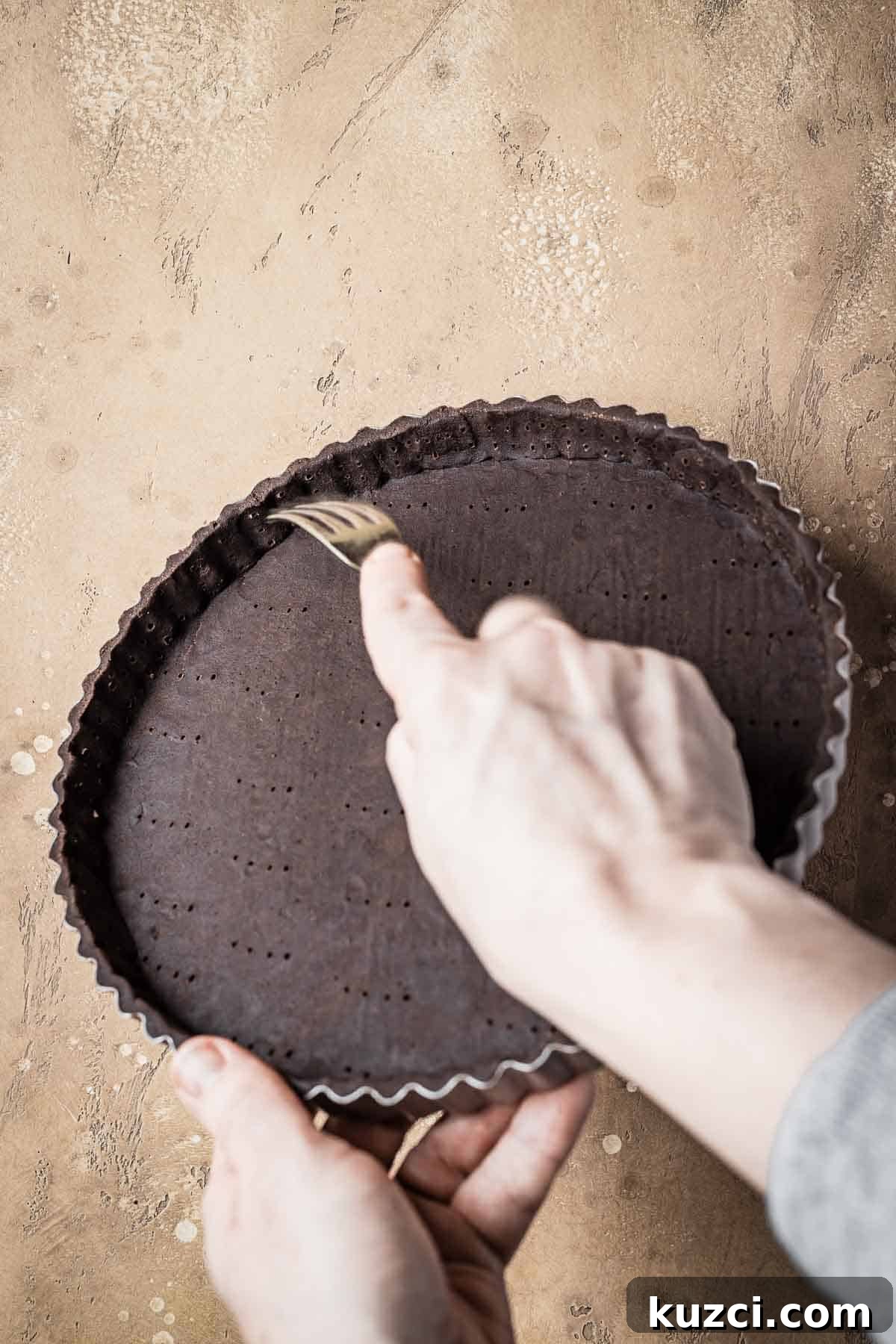 A hand docking the edges of an unbaked tart with a fork.