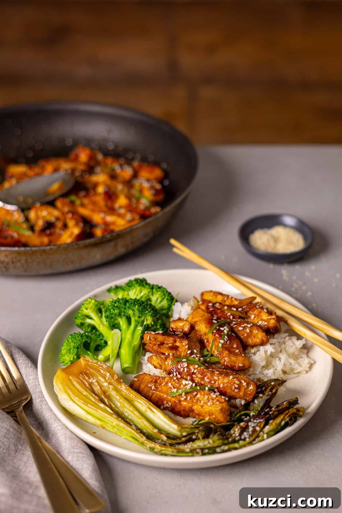 Honey Ginger Glazed Chicken Recipe 2 A serving of honey ginger chicken with rice and broccoli on a small plate and a skillet in the background with more chicken.
