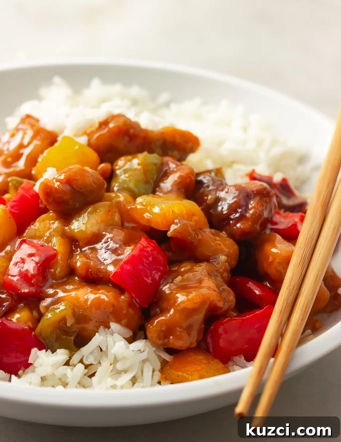 Crispy Sweet and Sour Chicken Recipe That Beats Takeout 2 A plate of sweet and sour chicken with bell peppers, onions, pineapples tossed in a sweet and savory sauce over rice.