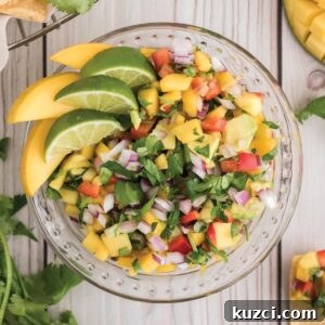 Fresh Mango Pico de Gallo Recipe 11 A overhead image of a bowl of fresh pico de gallo with mango with limes and mangoes as garnish.