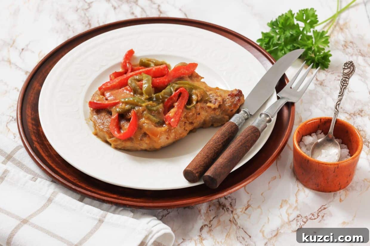 Smothered Pork Chops on a white plate, served with a fork and knife, next to a small bowl of salt and a sprig of parsley.