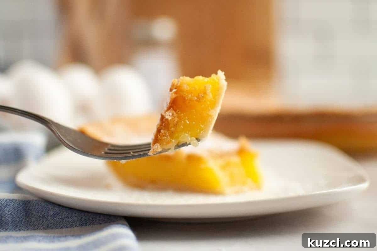 A fork holds a bite of Vinegar pie above a plate with a larger slice, with eggs and kitchen items blurred in the background.