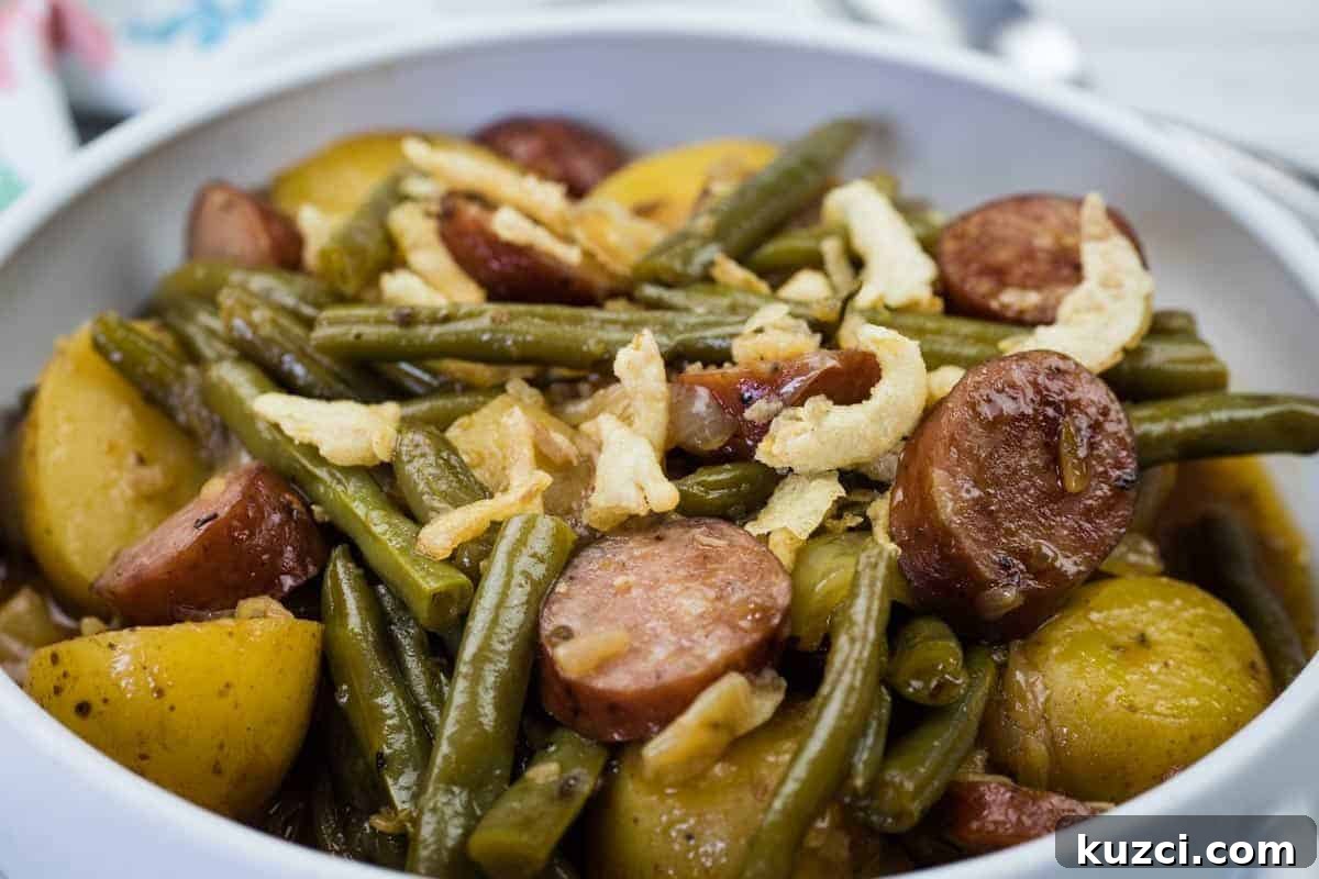 A bowl of Swamp Potatoes with cooked green beans, sliced sausage, and halved potatoes, topped with crispy fried onions.