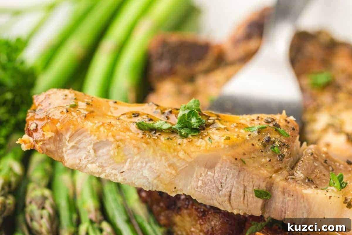A close-up of a seasoned pork chop slice garnished with herbs, held by a fork, with asparagus spears in the background.