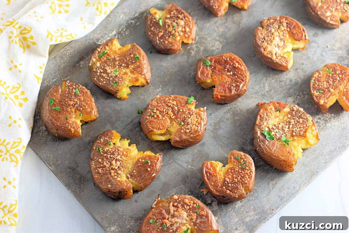 A baking sheet with several smashed roasted potatoes, garnished with herbs and grated cheese, arranged in rows.