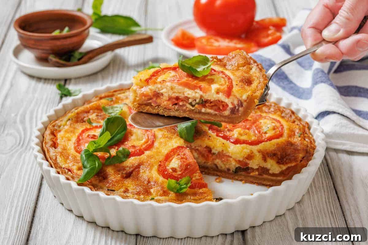 A slice of tomato pie being lifted with a serving utensil from a white fluted dish. A whole tomato pie is visible in the dish, garnished with tomato slices and basil.