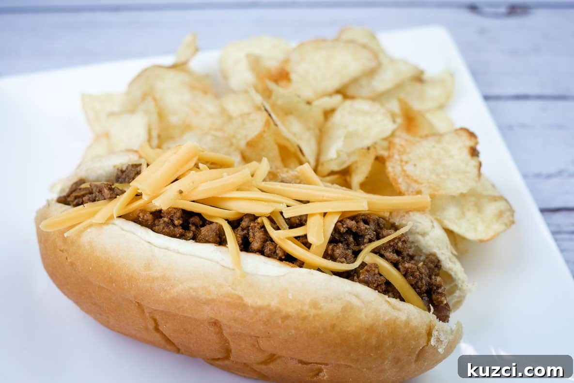 A hot dog chili topped with shredded cheddar, served with potato chips on a white plate.