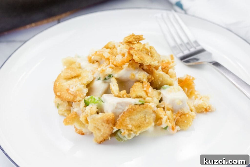A serving of Cheesy Ritz Cracker Chicken Casserole sits on a white plate next to a fork.