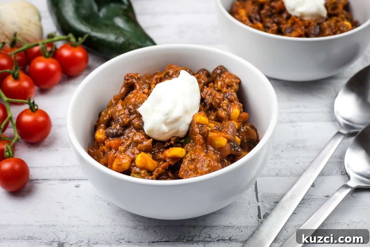 Two white bowls of Southwestern chili topped with sour cream are on a table.