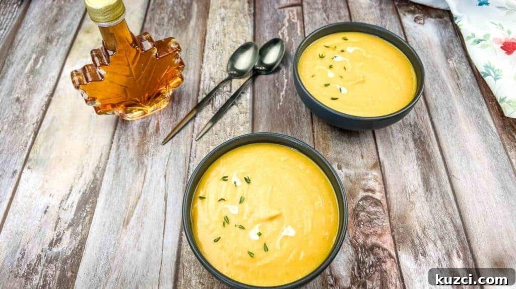 Two bowls of cream of butternut squash & sweet potato soup garnished with herbs on a wooden table.