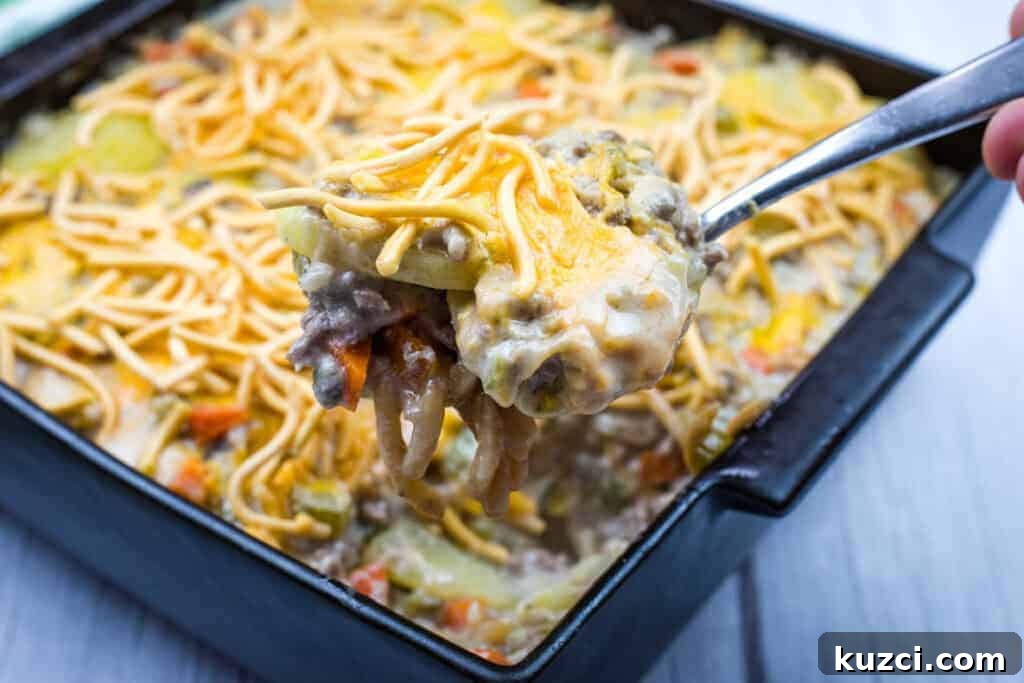 A close-up of a spoonful of Church Potluck Hot Dish with Chow Mein Noodles taken from a black square baking dish.