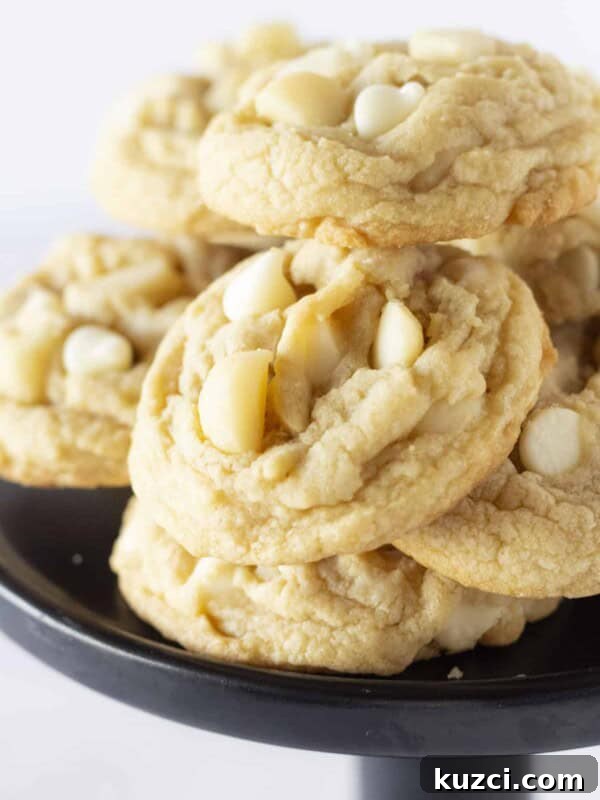 A black cake plate with a dozen of macadamia nut white chocolate chip cookies stacked on top.