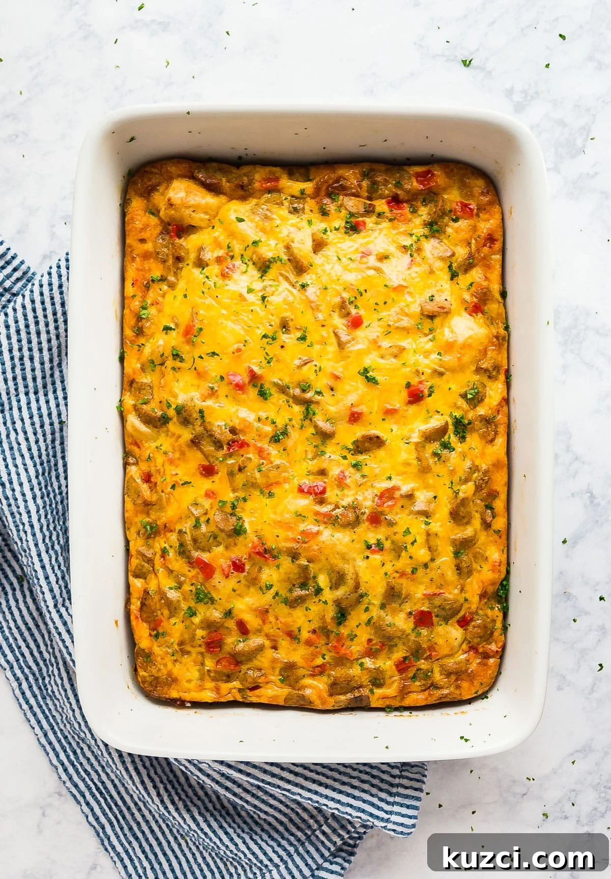 An overhead image of a breakfast casserole with biscuits in a white casserole dish with a blue and white striped napkin next to it.