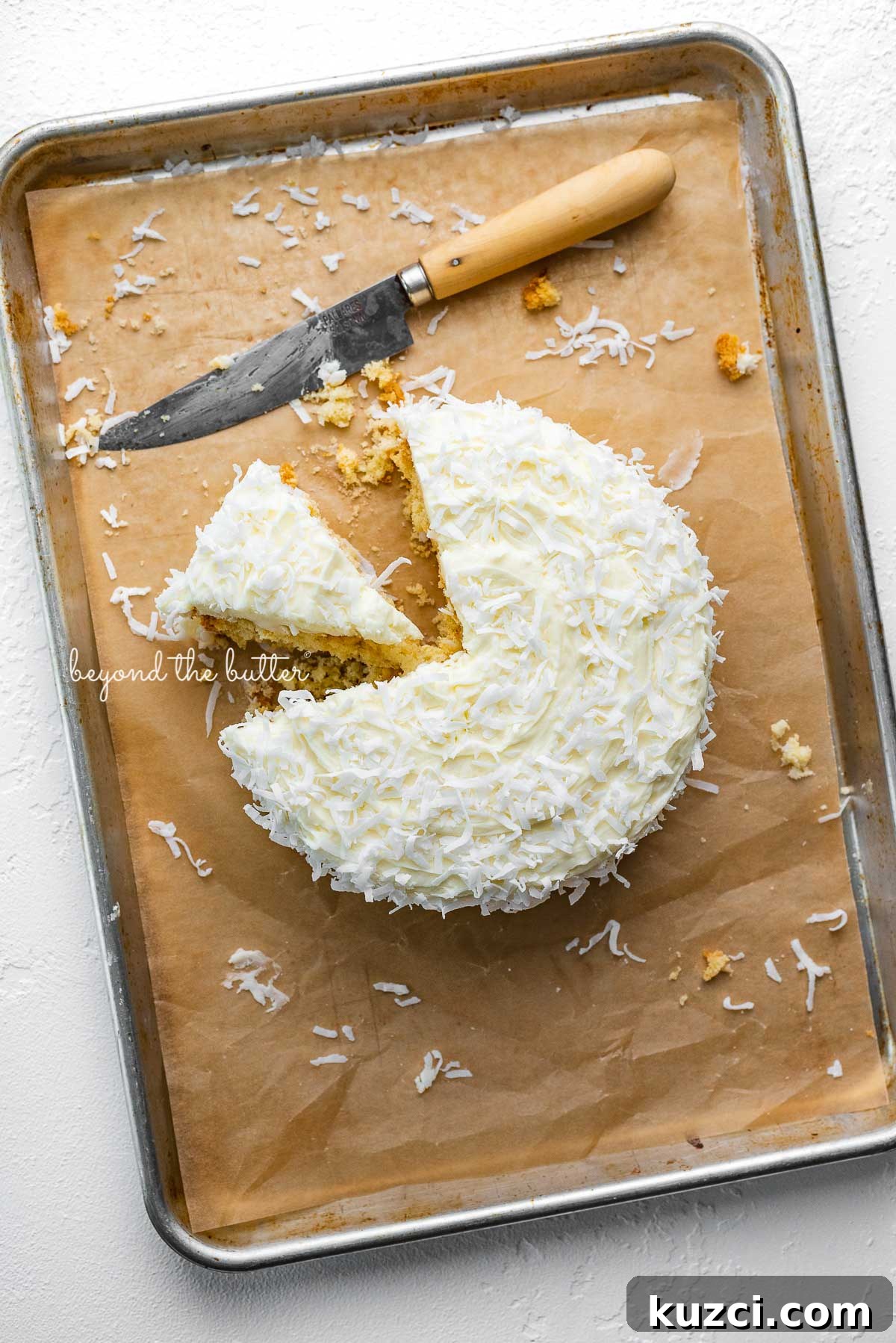 Moist Single Layer Coconut Cake Recipe 5 Single layer coconut cake frosted with coconut buttercream with slice cut out on natural parchment paper-lined baking sheet | © Beyond the Butter®