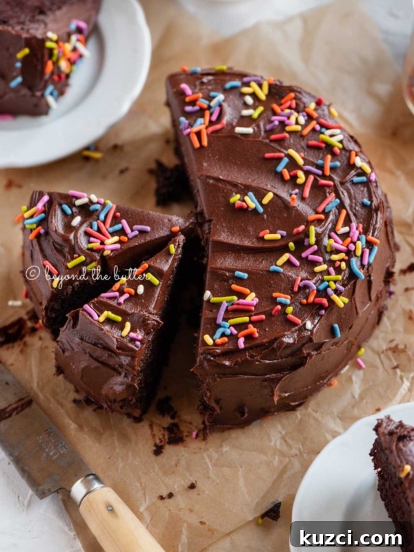 Moist Single Layer Coconut Cake Recipe 8 Angled image of sliced single layer chocolate cake on parchment paper with slices of cake on small dessert plates around it and a knife on parchment paper.