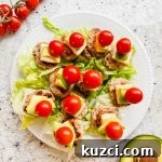 Simple Ground Turkey Recipes That Taste Delicious 18 lettuce underneath a mini turkey burger on a stick topped with cheese, avocado and a cherry tomato on white plate.