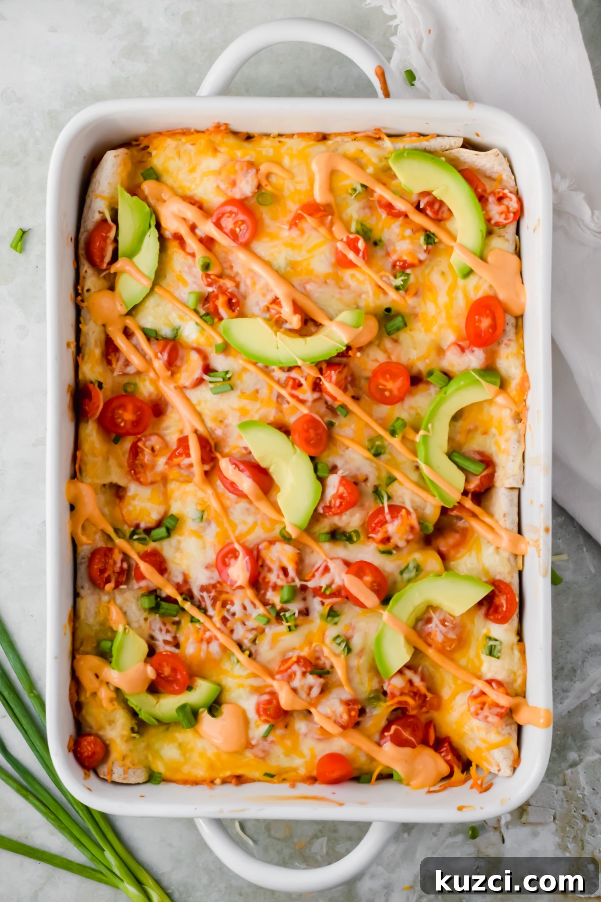 Simple Ground Turkey Recipes That Taste Delicious 3 baked healthy ground turkey enchiladas garnished with cherry tomato slices, avocado slices, green onion and queso in white baking pan.