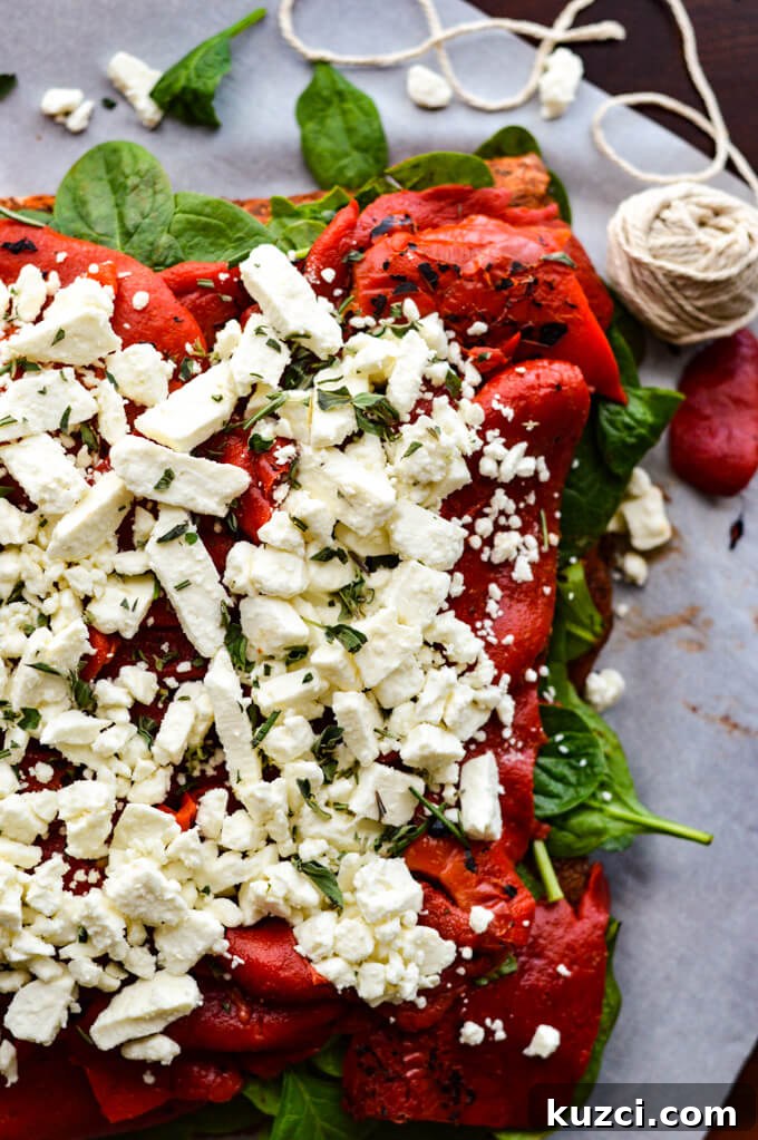 Stuffed Pork Roast with Roasted Red Peppers Feta and Spinach 3 A raw butterflied pork roast with spinach, roasted red peppers, and feta cheese on top.
