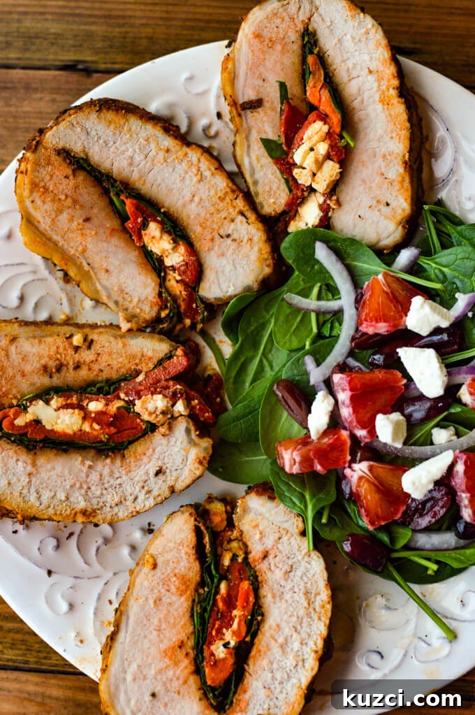 Stuffed Pork Roast with Roasted Red Peppers Feta and Spinach 8 Pork roast stuffed with roasted red peppers, feta, and spinach, sliced and served on a white plate with salad.