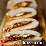 Pork roast stuffed with roasted red peppers, feta, and spinach, sliced and sitting on a wooden board.