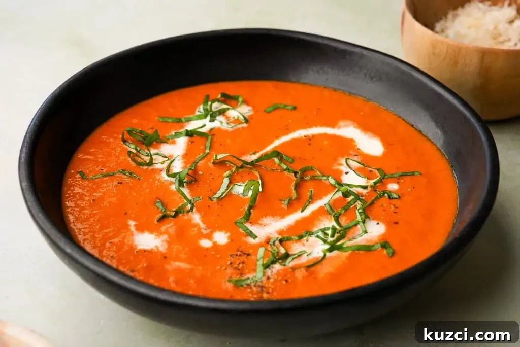 A creamy bowl of tomato bisque topped with freshly cracked black pepper and served with a golden, topped with fresh basil, pepper and cream