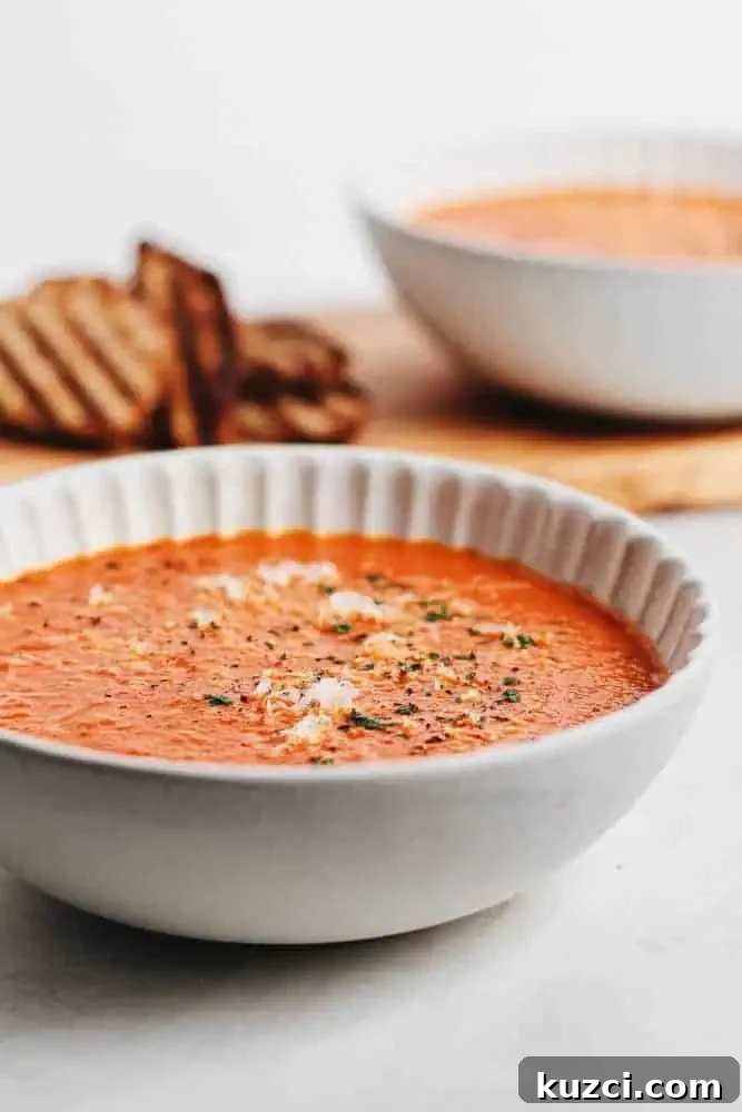 Creamy tomato bisque garnished with grated parmesan and cracked pepper, with grilled bread slices in the background.