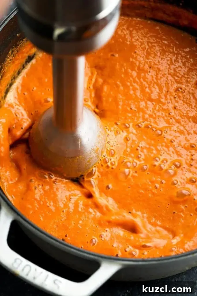 An immersion blender blending tomato bisque in a pot, creating a smooth, creamy texture.