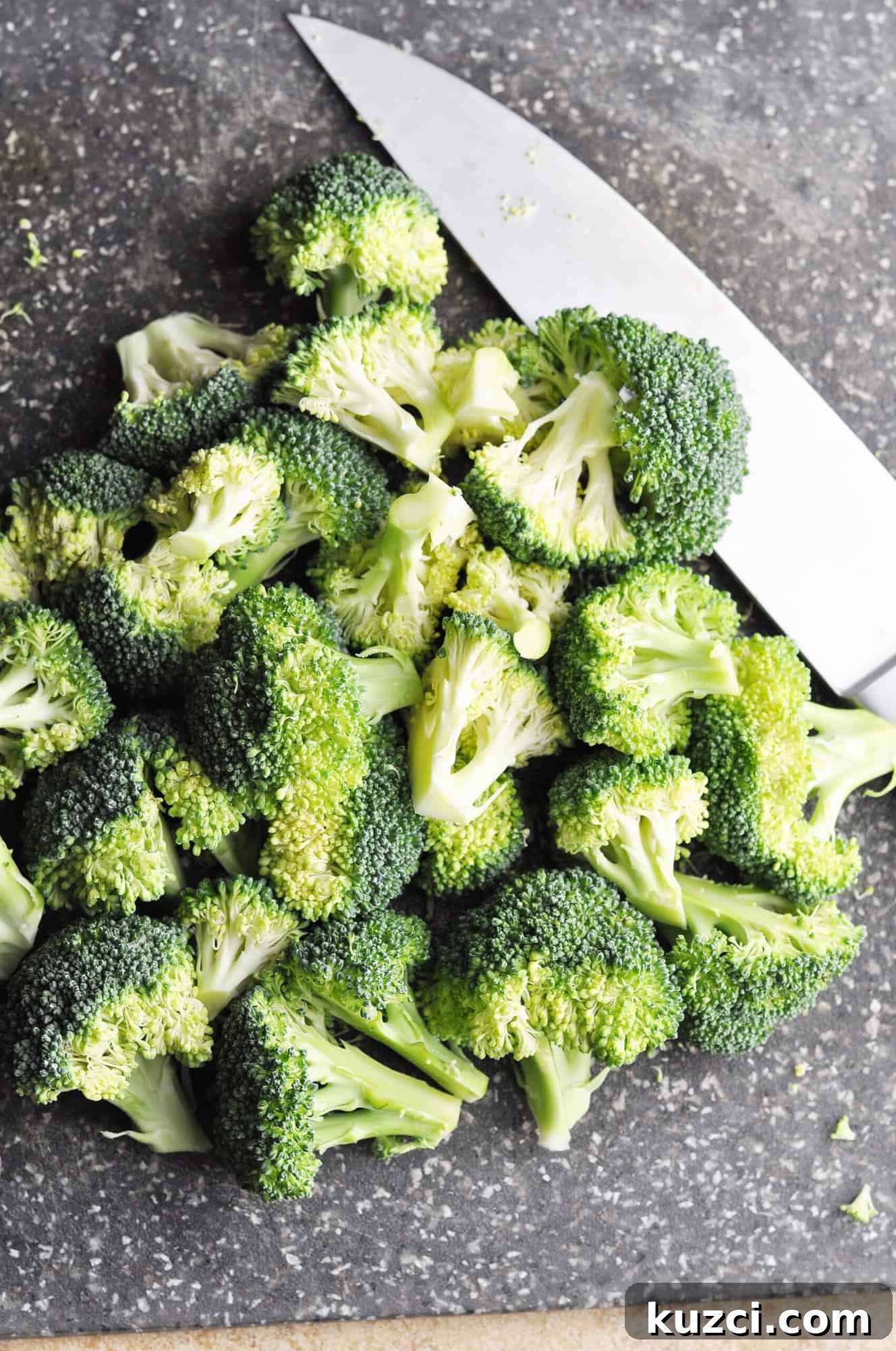 Chopped raw broccoli on cutting board with knife.