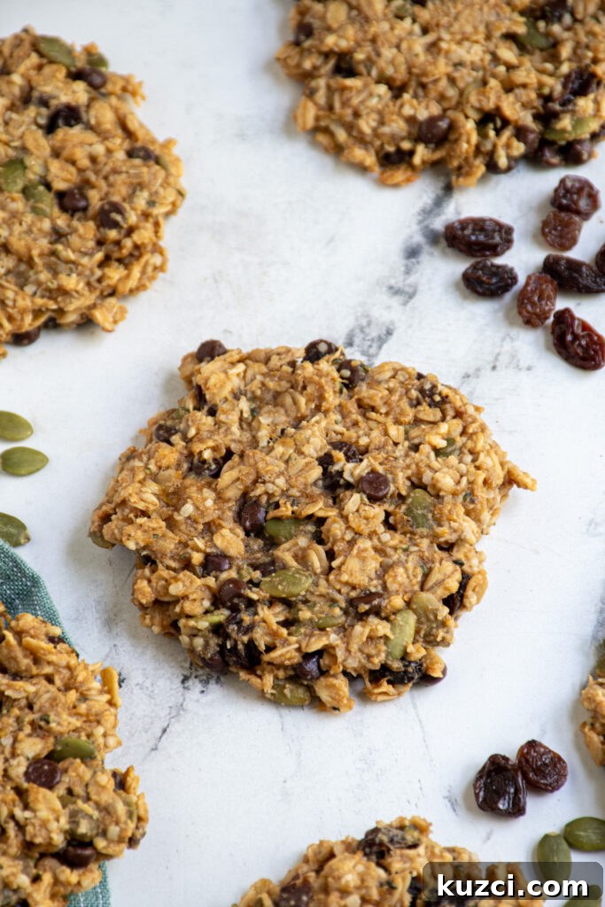 Protein-Packed Breakfast Cookies for Busy Mornings 7 Breakfast cookies on a tabletop with one in the center showing off fillings like raisins, pumpkin seeds, and mini chocolate chips.