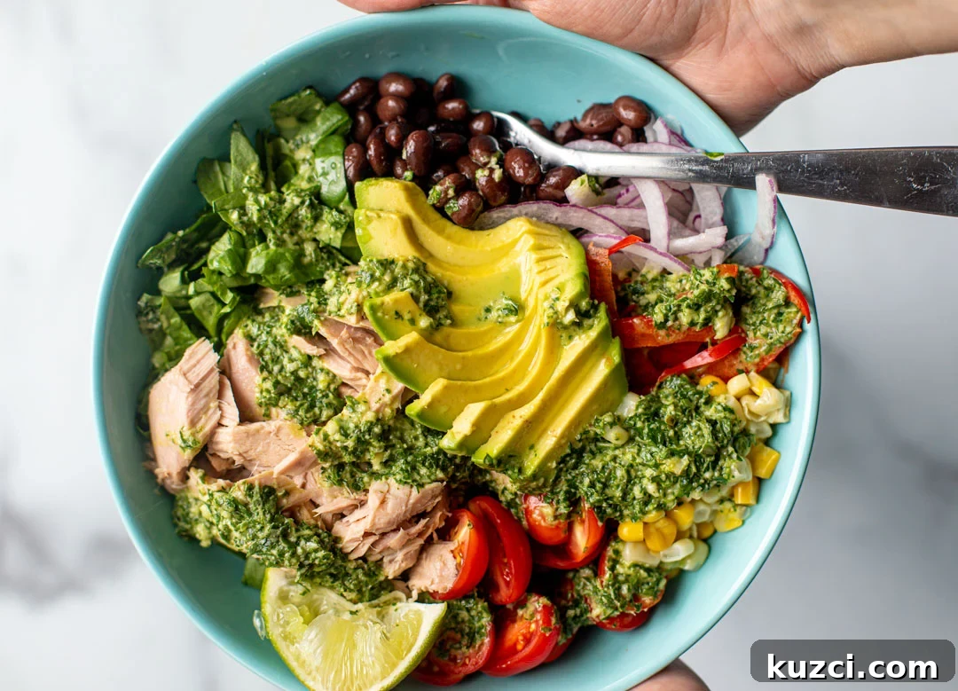 Colorful bowl of flaked tuna with vegetables and an herb dressing drizzled on top.