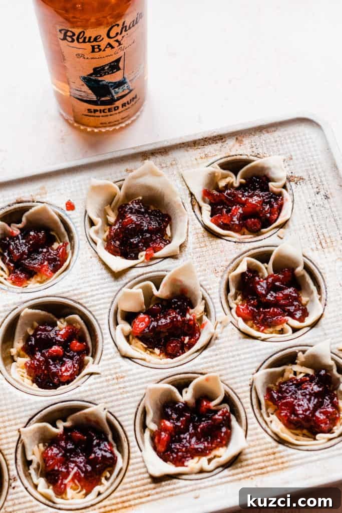 Gouda Puff Pastry Bites with Spiced Rum Cranberry Sauce 5 A muffin tin filled with unbaked puff pastry bites, with a bottle of spiced rum in the background