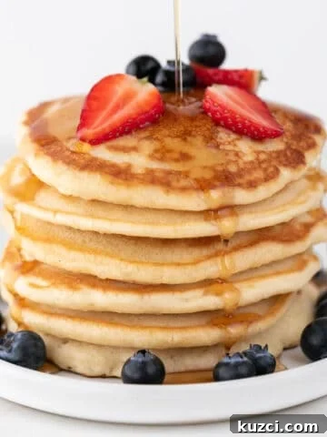 Vegan pancakes heaped with strawberries, blueberries, and maple syrup drizzle.