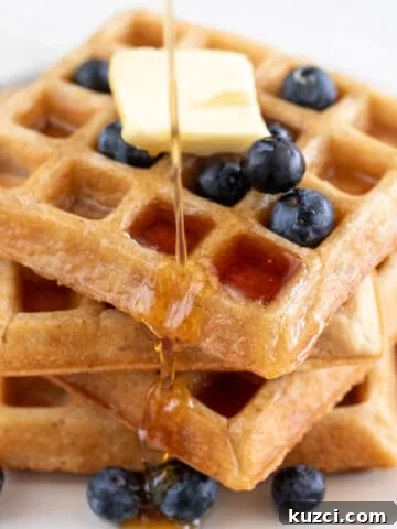 A tower of fluffy vegan waffles topped with blueberries and maple syrup.