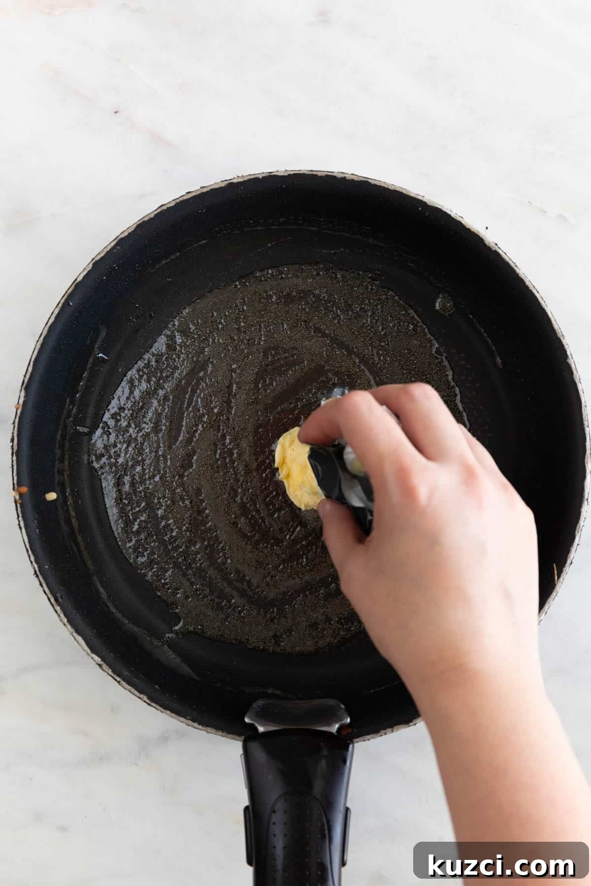 A hand rubbing a vegan butter stick on a pan.