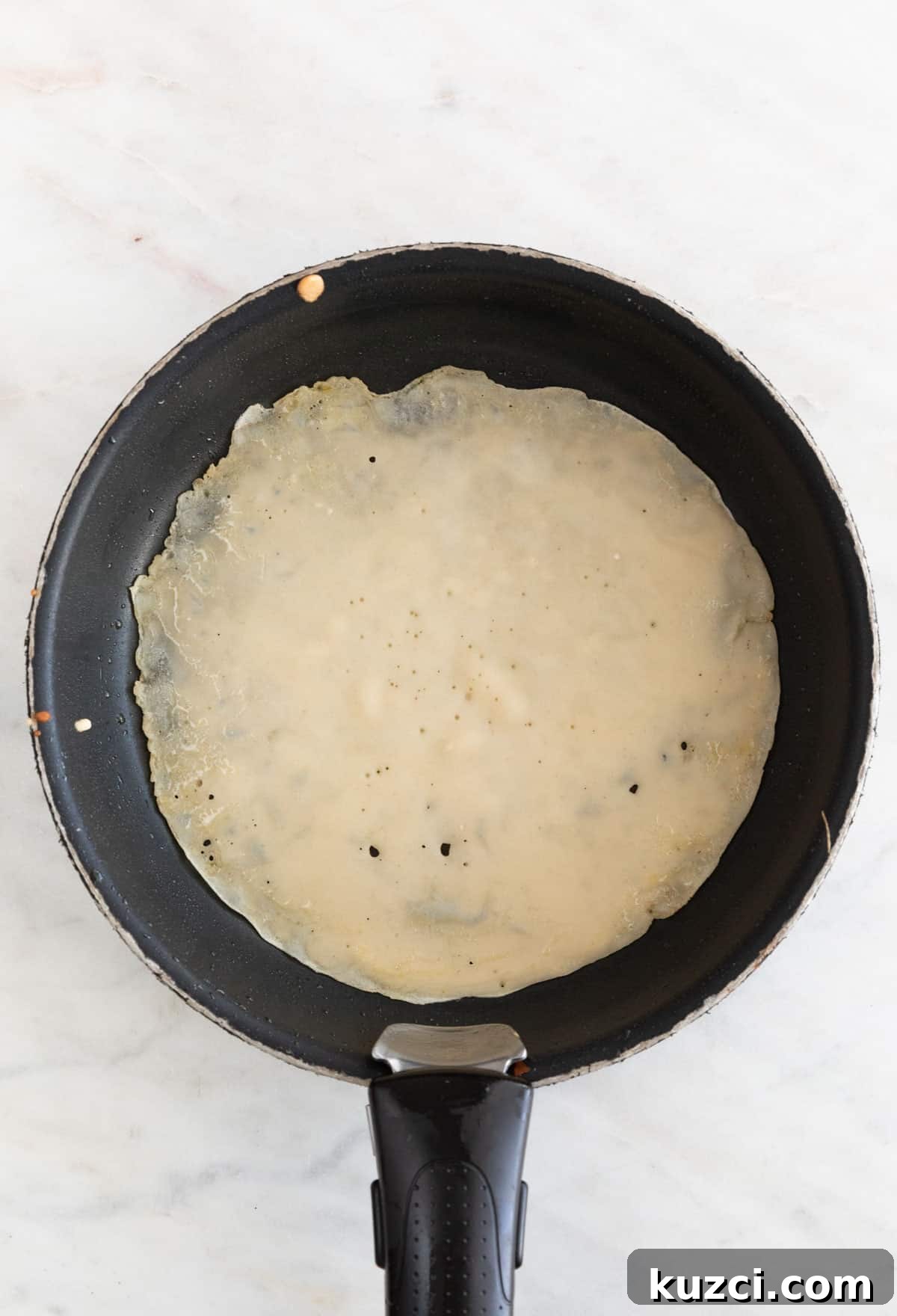 A skillet with a crepe cooked on one side.