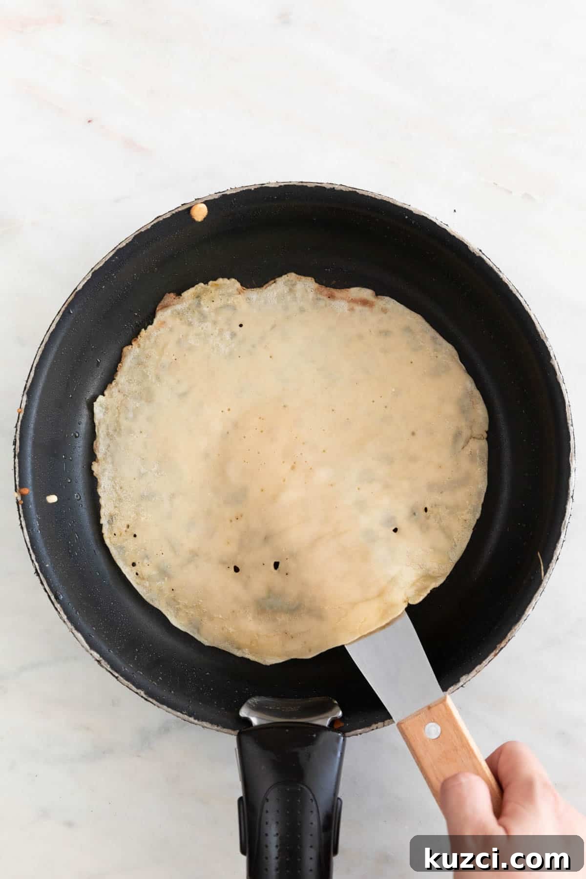 A hand with a butter knife flipping a crepe.
