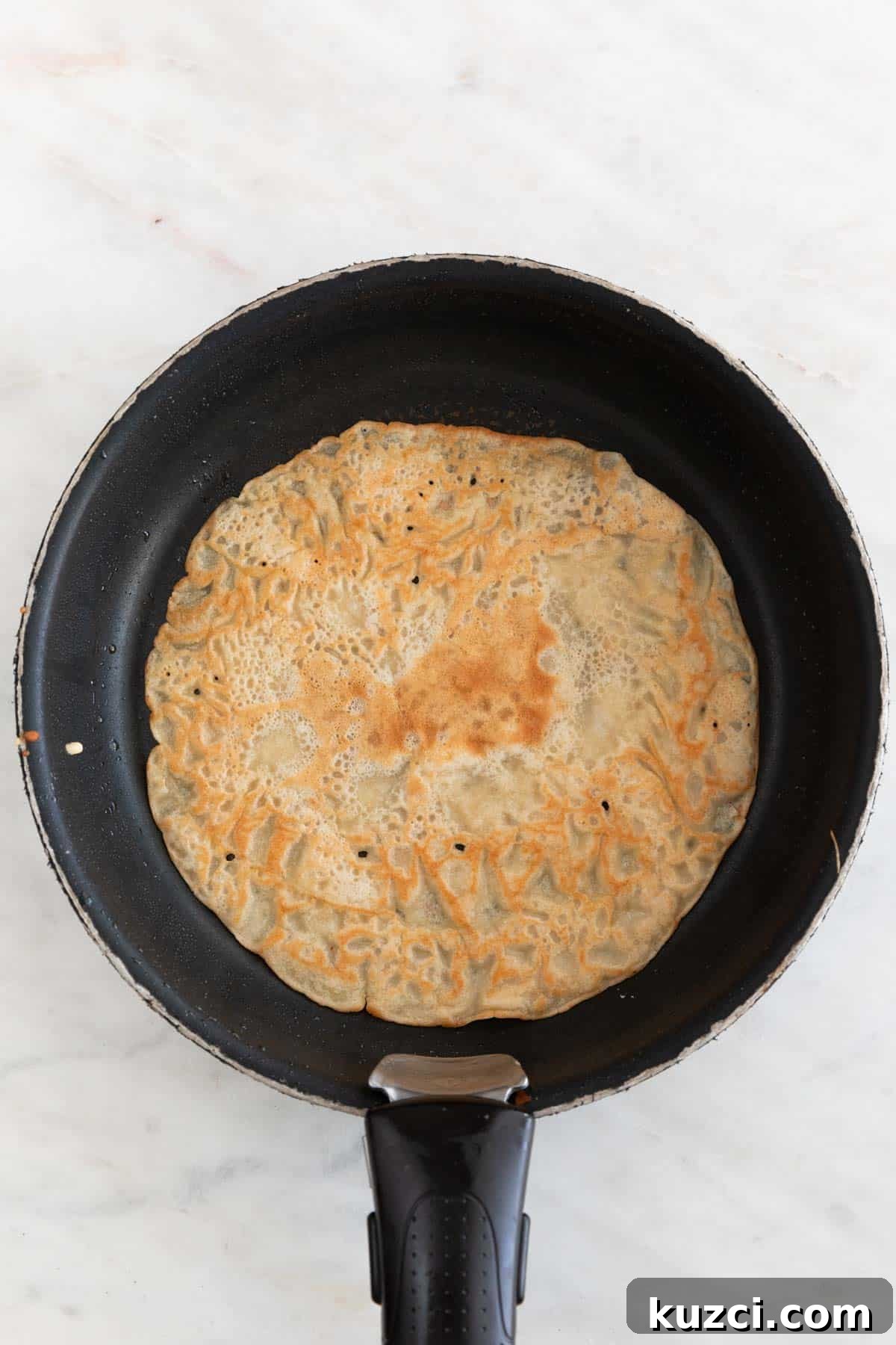 A skillet with a crepe cooked on both sides.