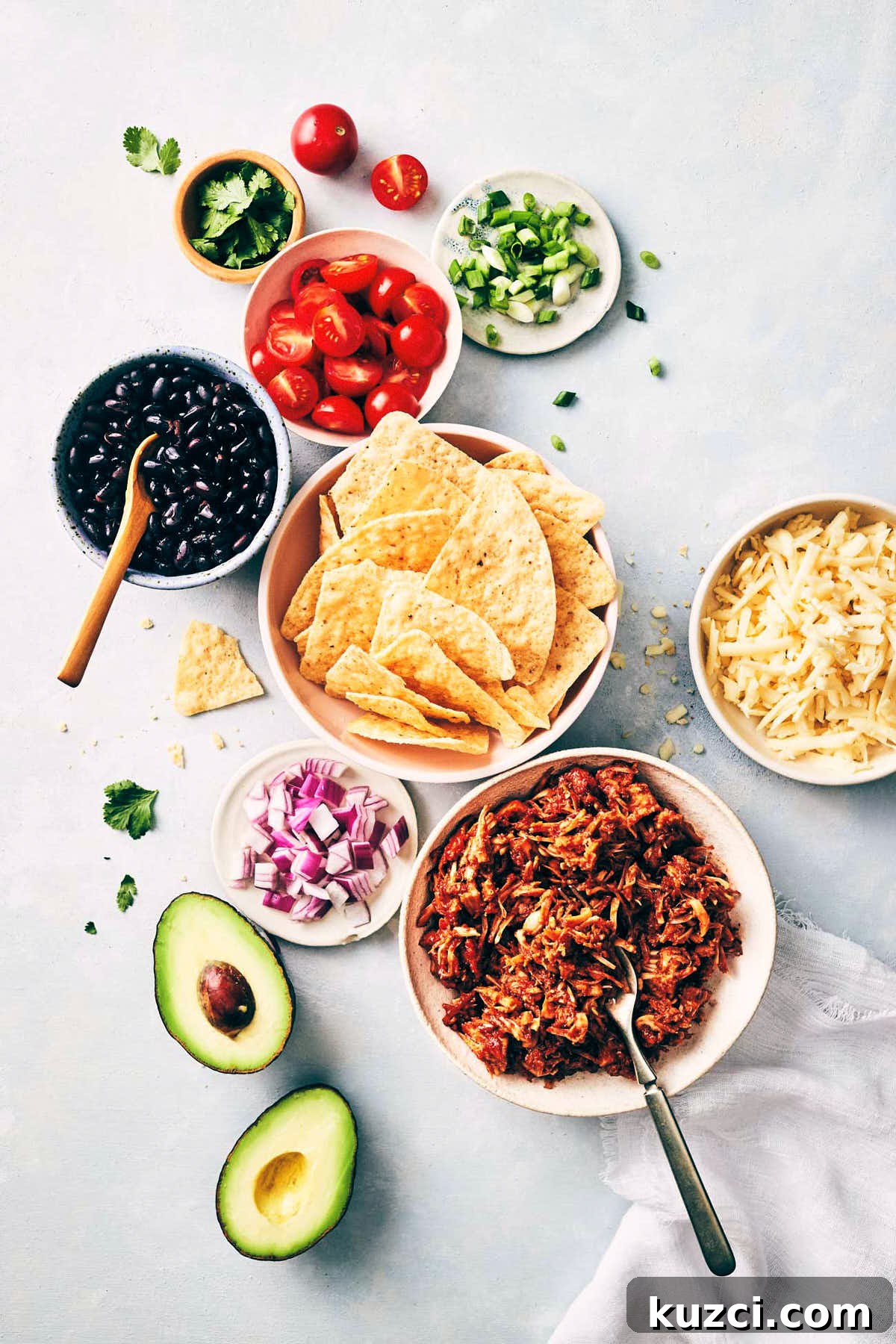 Plant-Based Pulled Pork Nachos 5 Ingredients for pulled pork nachos like avocado, vegan pulled pork, black beans, red onions and tortilla chips laid out on the counter before assembly