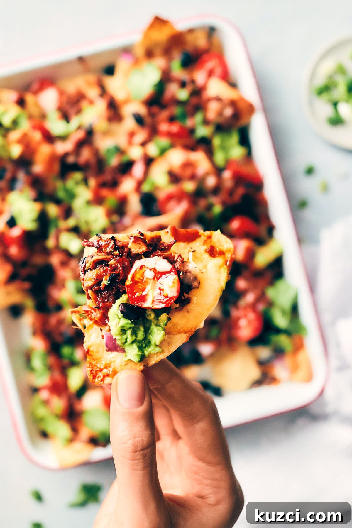 Plant-Based Pulled Pork Nachos 7 Close on on a single chip topped with vegan pulled pork, tomato, black beans and avocado