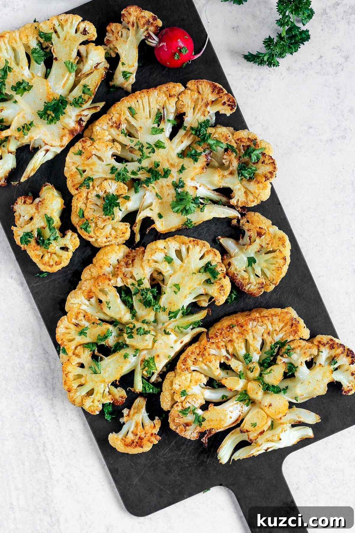 Roasted cauliflower steaks sprinkled with fresh parsley on a black cutting board.