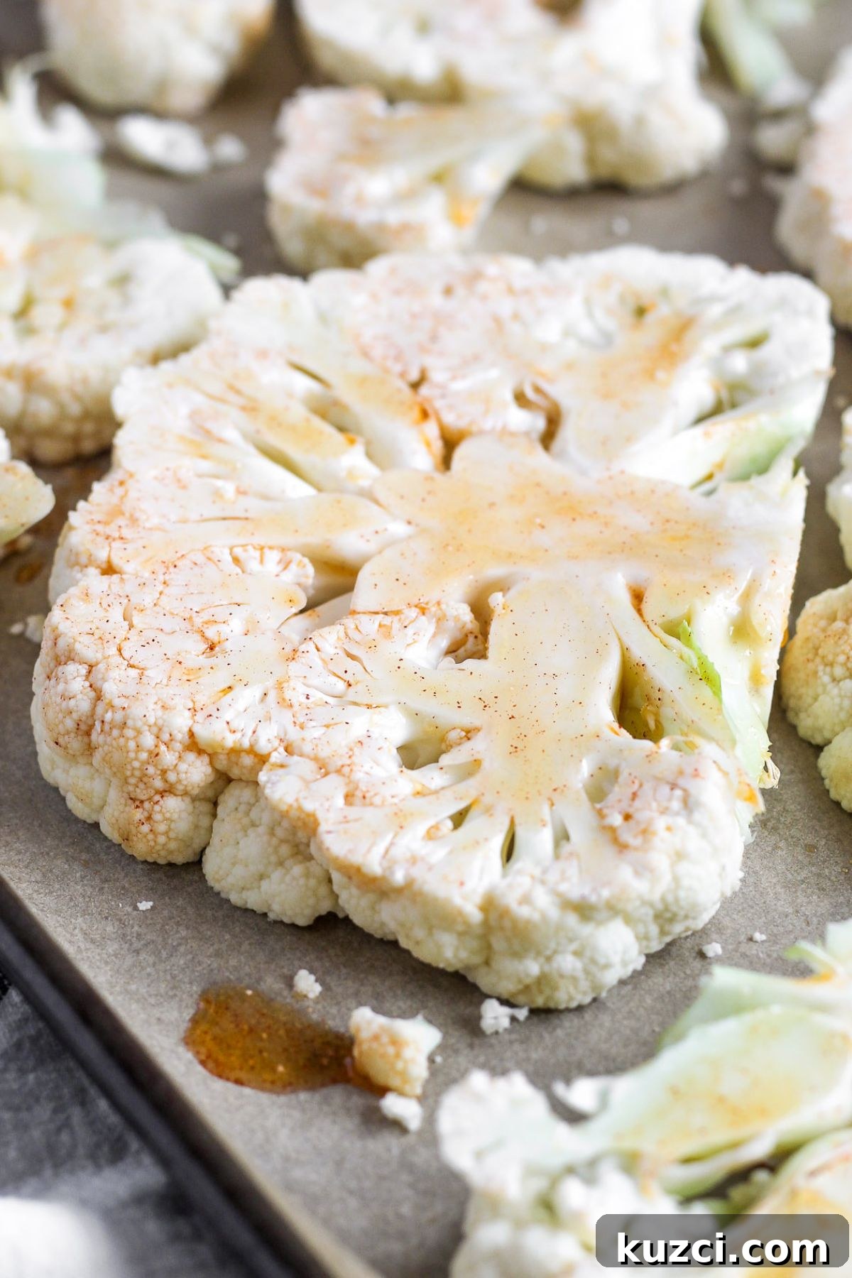 Raw cauliflower steaks on a baking sheet brushed with olive oil marinade.