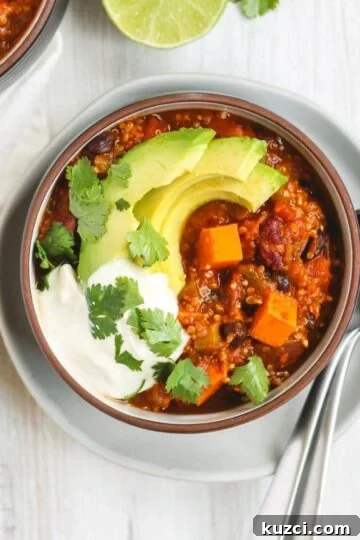 Vegetarian sweet potato topped with avocado, cilantro, and sour cream in a dark bowl sitting on a white plate.