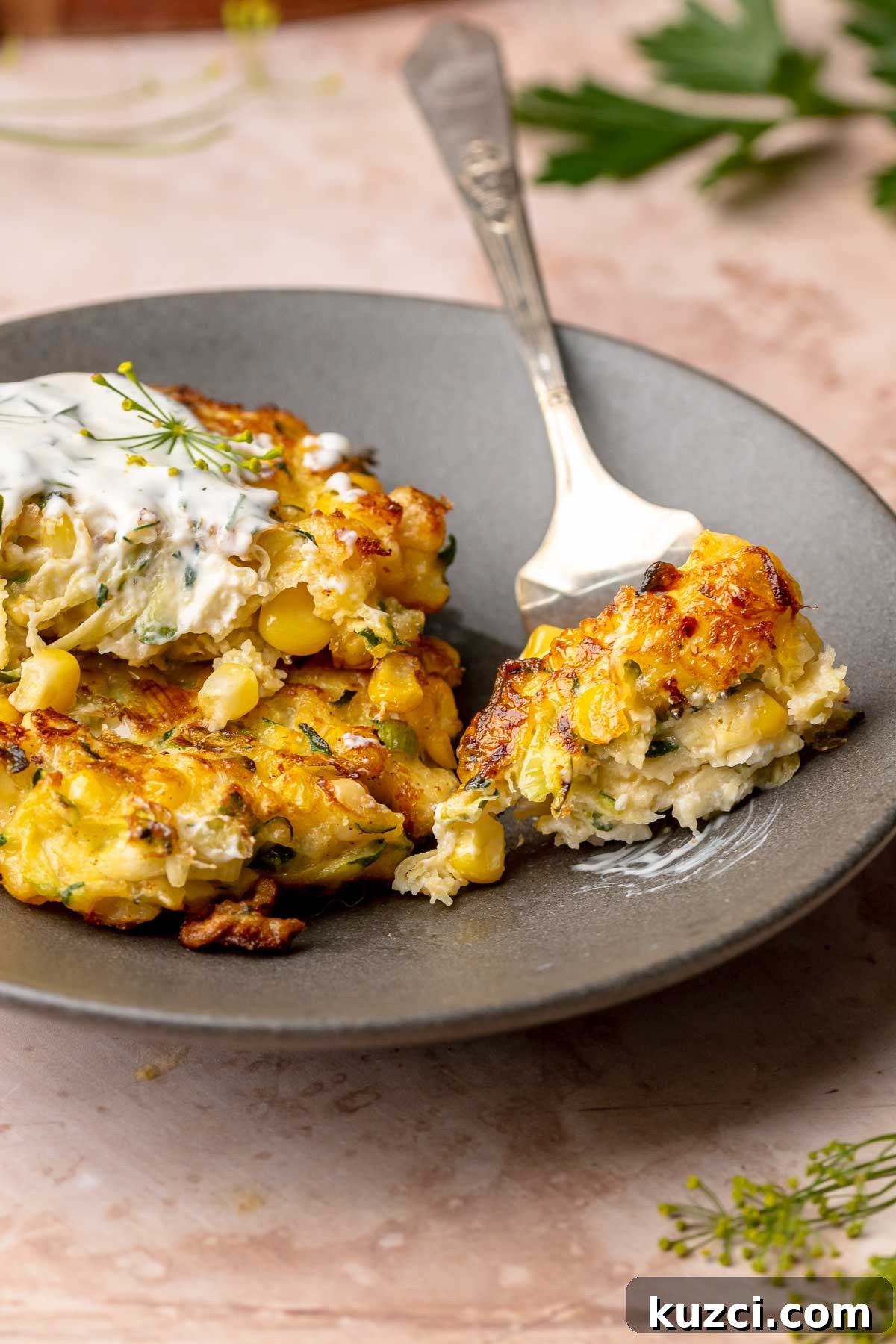 Crispy Corn and Zucchini Fritters with Herbed Yogurt Sauce 11 A fork holds a piece of fritter on a plate.