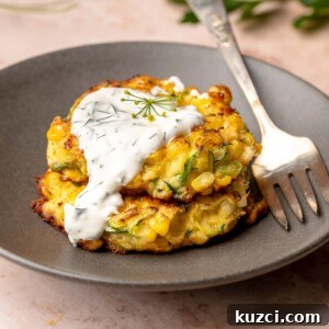 Crispy Corn and Zucchini Fritters with Herbed Yogurt Sauce 16 A stack of two corn and zucchini fritters on a plate with yogurt sauce dripping down the side.