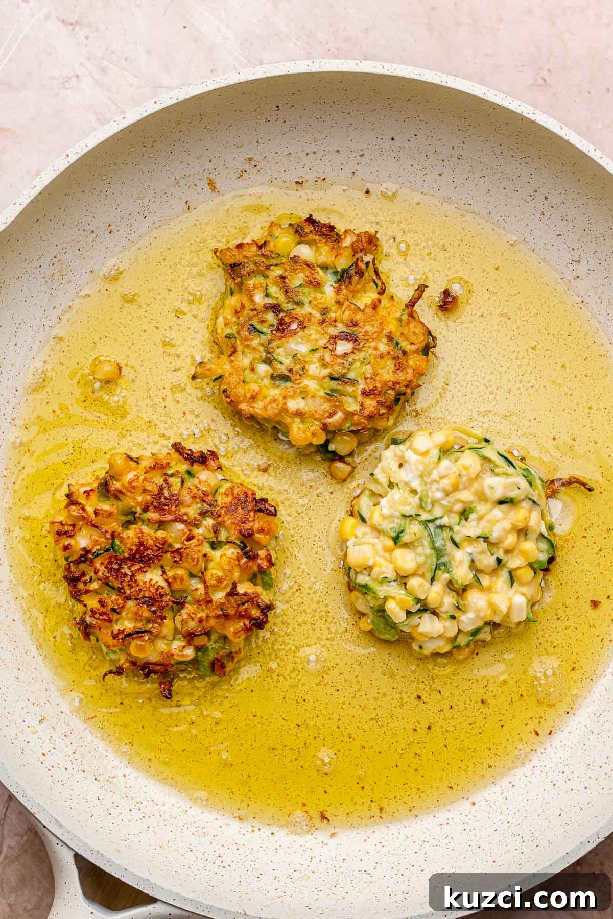 Crispy Corn and Zucchini Fritters with Herbed Yogurt Sauce 10 Corn and zucchini fritters frying in a pan.