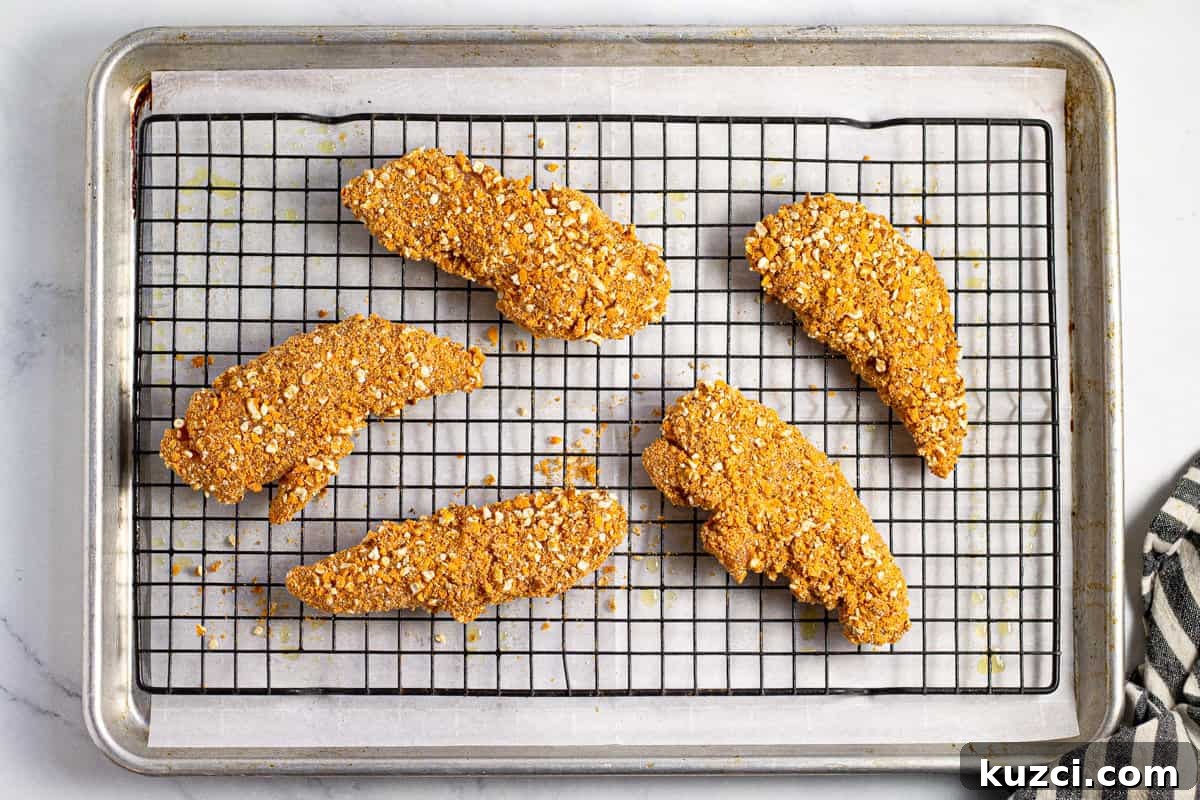 Crispy Oven Fried Chicken Tenders 8 Breaded chicken tenders on a cooling rack on a parchment lined baking sheet